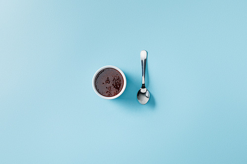 top view of teaspoon near jam in bowl on blue background