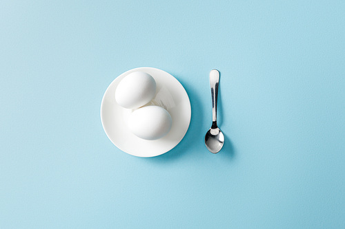 top view of teaspoon near boiled eggs on white plate on blue background