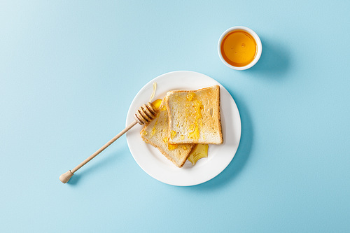 top view of toasts with honey and wooden dipper on white plate on blue background