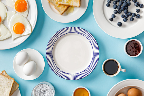 top view of served breakfast with empty plate in middle on blue background