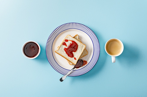 top view of toasts, spoon, bowl with jam and cup of coffee on blue background