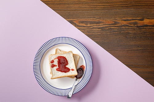 top view of toasts, spoon with jam on violet and wooden background