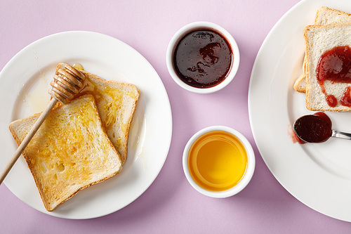 top view of toasts with jam and honey, bowls and wooden dipper on violet background