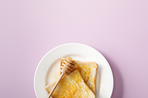 top view of toasts with honey and wooden dipper on white plate on violet background