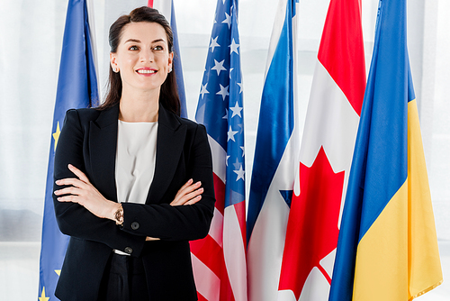 happy diplomat standing with crossed arms near flags