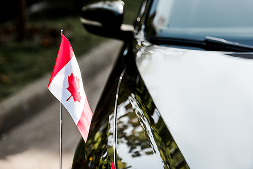 selective focus of canadian flag with maple leaf on black car