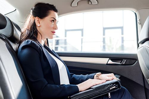 side view of attractive ambassador holding briefcase while sitting in car