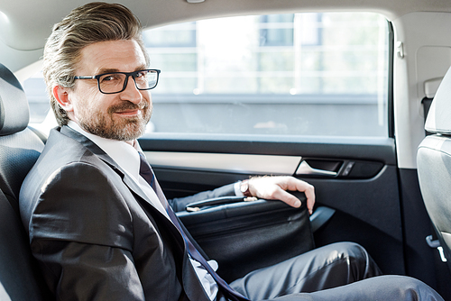 happy diplomat in glasses sitting with briefcase in car