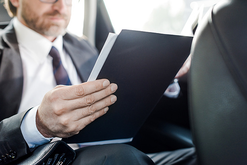 selective focus of bearded diplomat holding folder in car