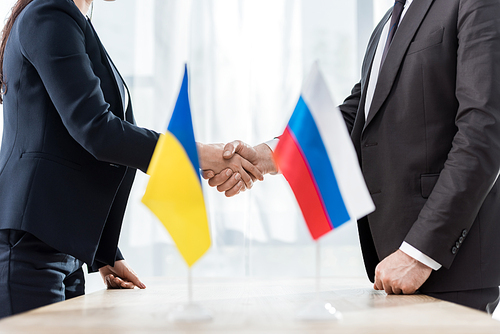 cropped view of diplomats in formal wear shaking hands near ukrainian and russian flags