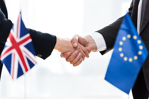 cropped view of diplomats shaking hands near european union and united kingdom flags