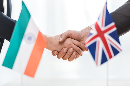cropped view of diplomats shaking hands near flags of india and united kingdom