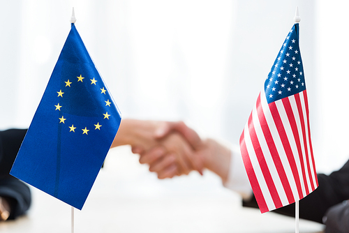 selective focus of flags of usa and european union near diplomats shaking hands