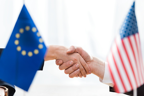 selective focus of diplomats shaking hands near flags of usa and european union