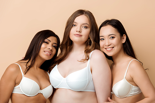 happy and overweight multicultural women in bras isolated on beige