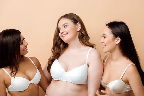cheerful and overweight multicultural women in bras isolated on beige