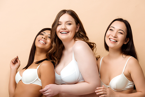 cheerful plus size multicultural women in bras isolated on beige