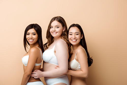 cheerful plus size multicultural girls in bras isolated on beige