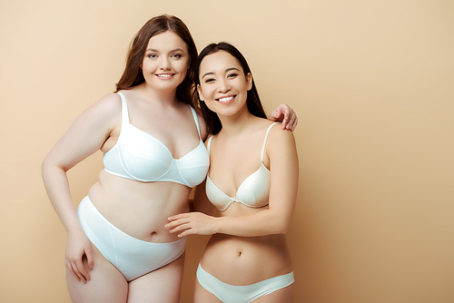 plus size woman smiling with asian girl in underwear isolated on beige, body positive concept