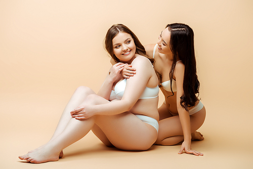 asian girl hugging happy overweight woman in underwear while sitting on beige, body positive concept