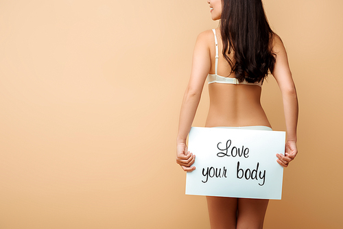 cropped view of happy girl holding placard with love your body lettering isolated on beige