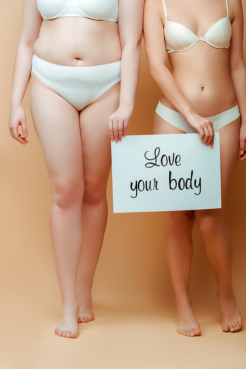 Cropped view of women with placard with love your body lettering on beige background