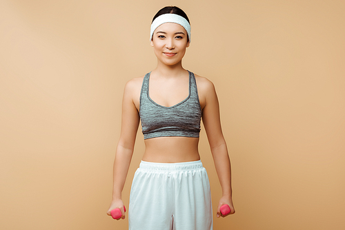 Asian sportswoman with dumbbells smiling and  on isolated on beige
