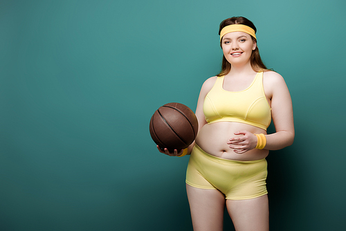 Plus size sportswoman with ball  and smiling on green background