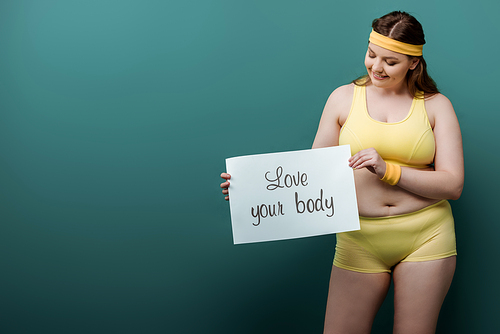 Plus size sportswoman smiling and looking at placard with love your body lettering on green