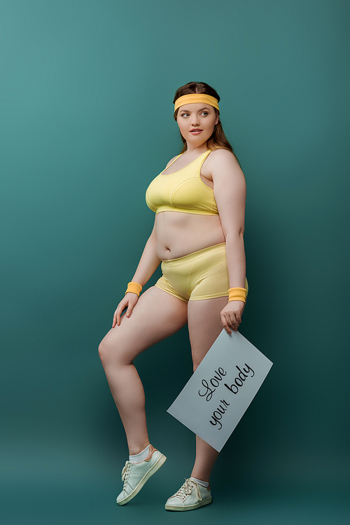 Plus size sportswoman with placard with love your body lettering looking away on green background