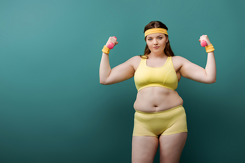 Plus size sportswoman  with dumbbells on green background