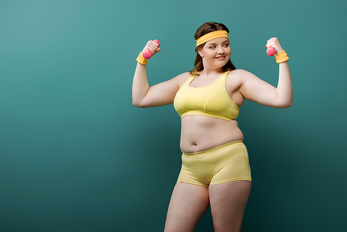 Plus size sportswoman smiling and looking at dumbbell on green