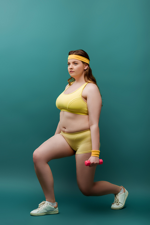 Plus size sportswoman training with dumbbells on green background