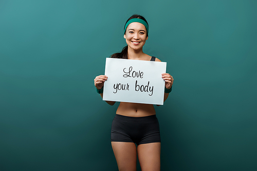 Asian sportswoman , smiling and showing placard with love your body lettering on green
