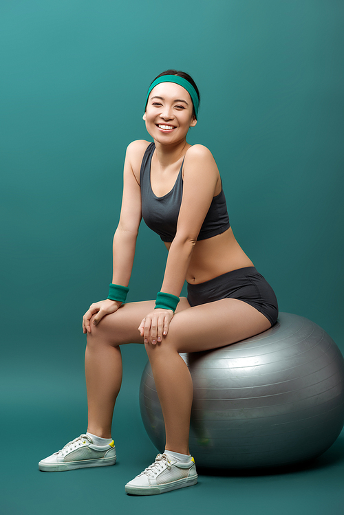 Happy asian sportswoman smiling and  on fitness ball on green background