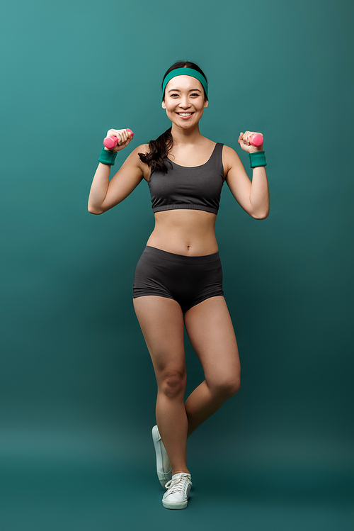 Happy asian sportswoman training with dumbbells smiling and  on green background