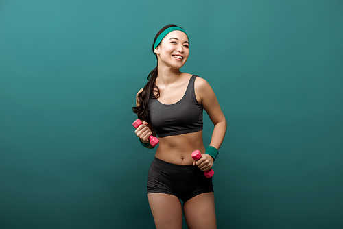 Happy asian sportswoman with dumbbells smiling isolated on green