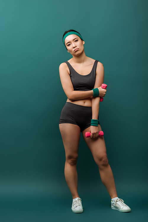 Tired asian sportswoman with dumbbells  on green background