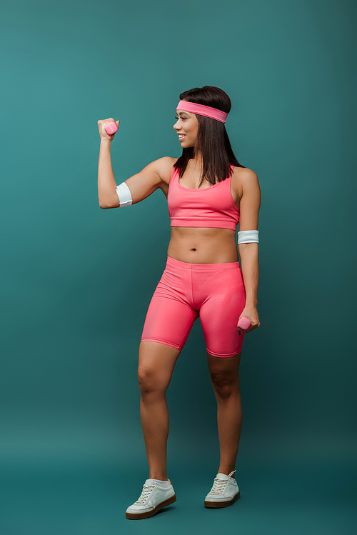 African american sportswoman smiling and looking at dumbbell on green background