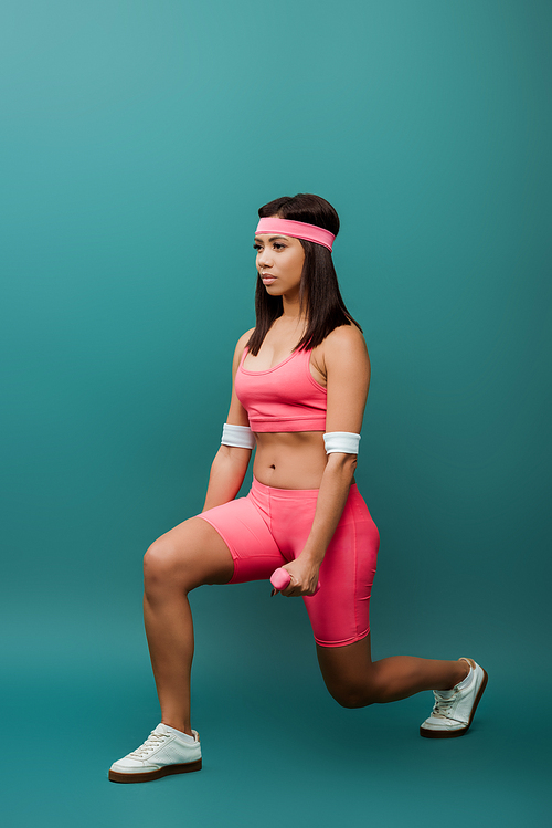 African american sportswoman doing lunges with dumbbells on green background