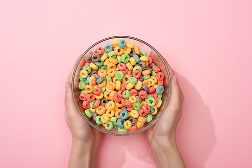 cropped view of woman holding bright colorful breakfast cereal in bowl on pink background