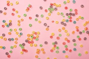 top view of bright multicolored breakfast cereal scattered on pink background