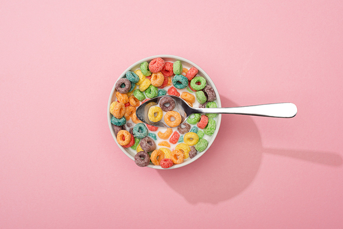 top view of bright colorful breakfast cereal in bowl with spoon on pink background