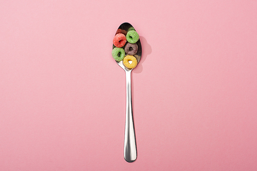 top view of bright colorful breakfast cereal in spoon on pink background