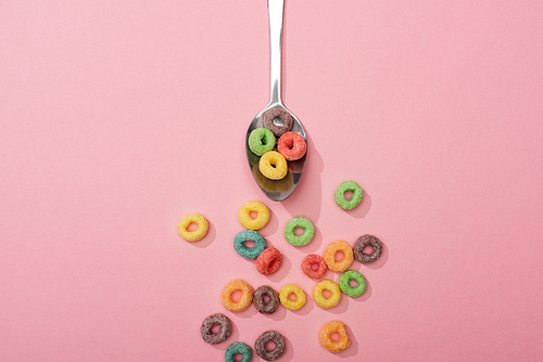 top view of bright colorful breakfast cereal scattered from spoon on pink background