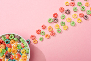 top view of bright colorful breakfast cereal with milk in bowl and around on pink background