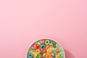 top view of bright colorful breakfast cereal with milk in bowl on pink background
