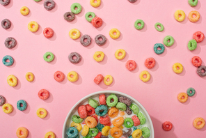 top view of bright colorful breakfast cereal with milk in bowl and on pink background