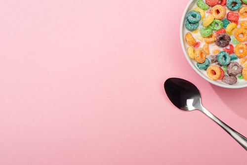 top view of bright colorful breakfast cereal with milk in bowl near spoon on pink background