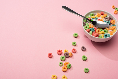 bright colorful breakfast cereal with milk in bowl with spoon on pink background